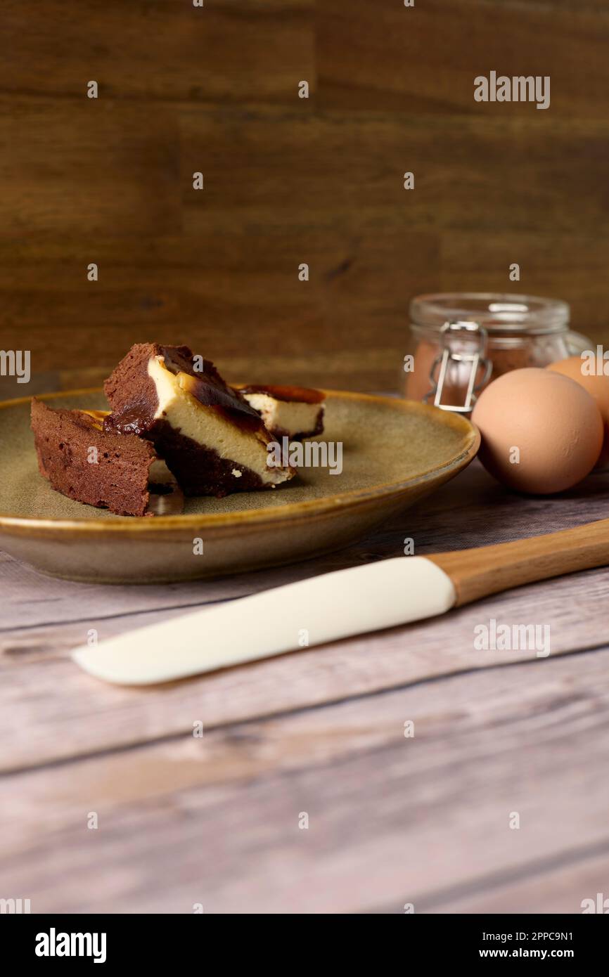 Homemade brownie chocolate cheesecake on a wood background with eggs, cacao and spatula Stock Photo