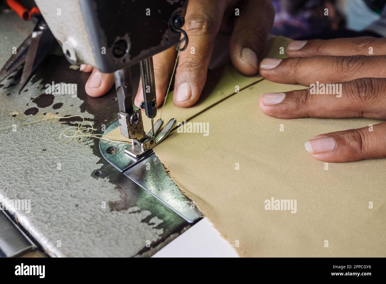 Stitching fabric on professional manufacturing machine at workplace. Close up view of sewing process. Tailoring at the factory. Blurred background. Stock Photo