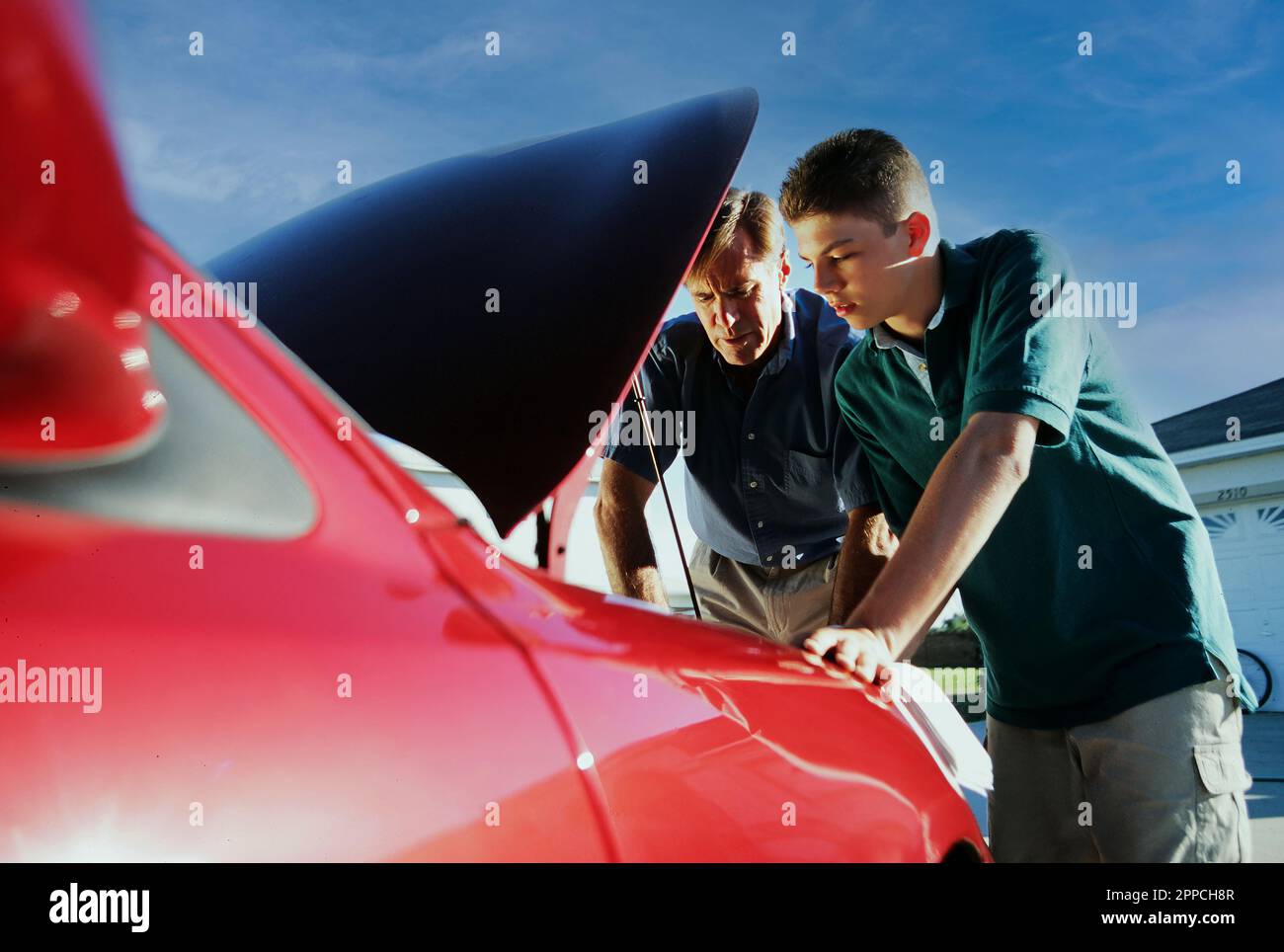 Father and son looking under the hood of the teenager's new car Stock Photo