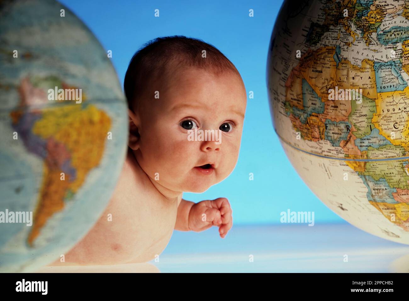 Studio portrait of a very curious baby crawling between two globes Stock Photo