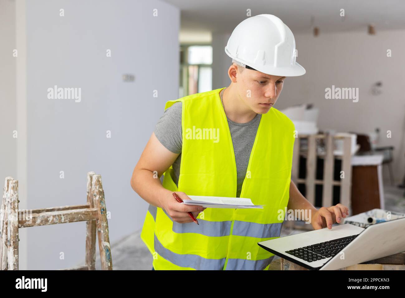 Teenage boy using laptop and checking documentation in construction ...