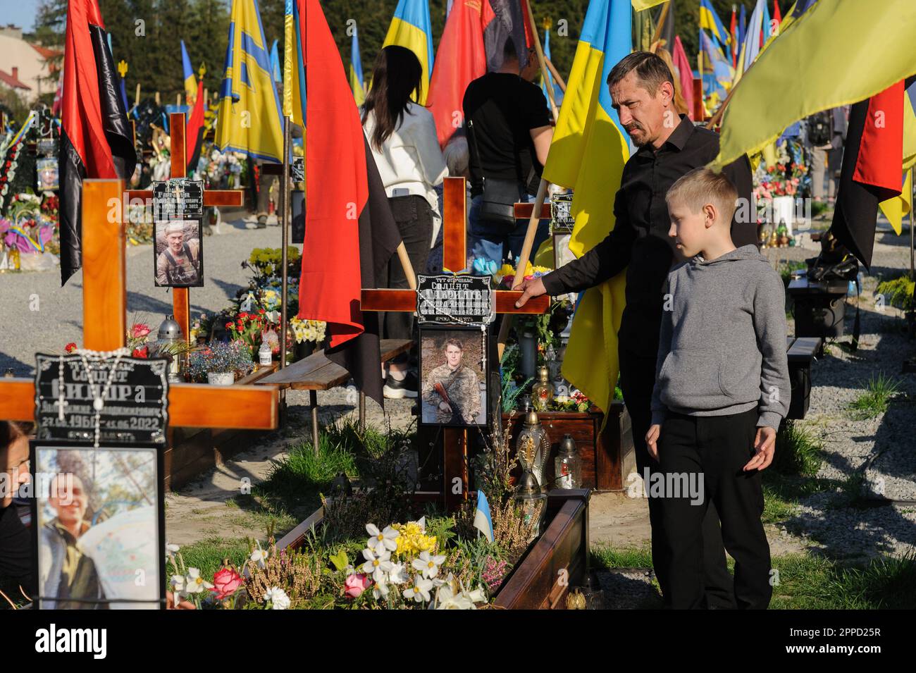Lviv, Ukraine 23 April 2023. People stand at graves in the Mars field at Lychakiv cemetery. Heroes of the Ukraine, servicemen who defended the territory of Ukraine are buried here. Russia invaded Ukraine on 24 February 2022, triggering the largest military attack in Europe since World War II. Stock Photo