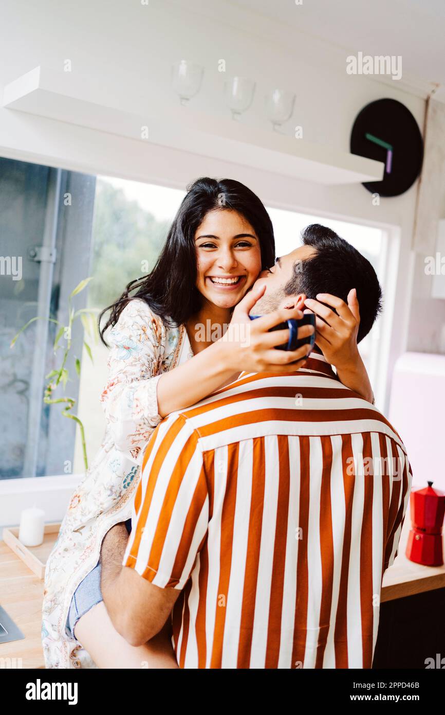 Man kissing happy girlfriend in kitchen at home Stock Photo