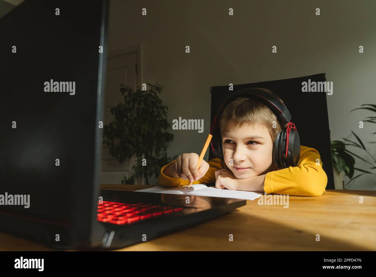 Boy wearing headset studying online through laptop at home Stock Photo ...