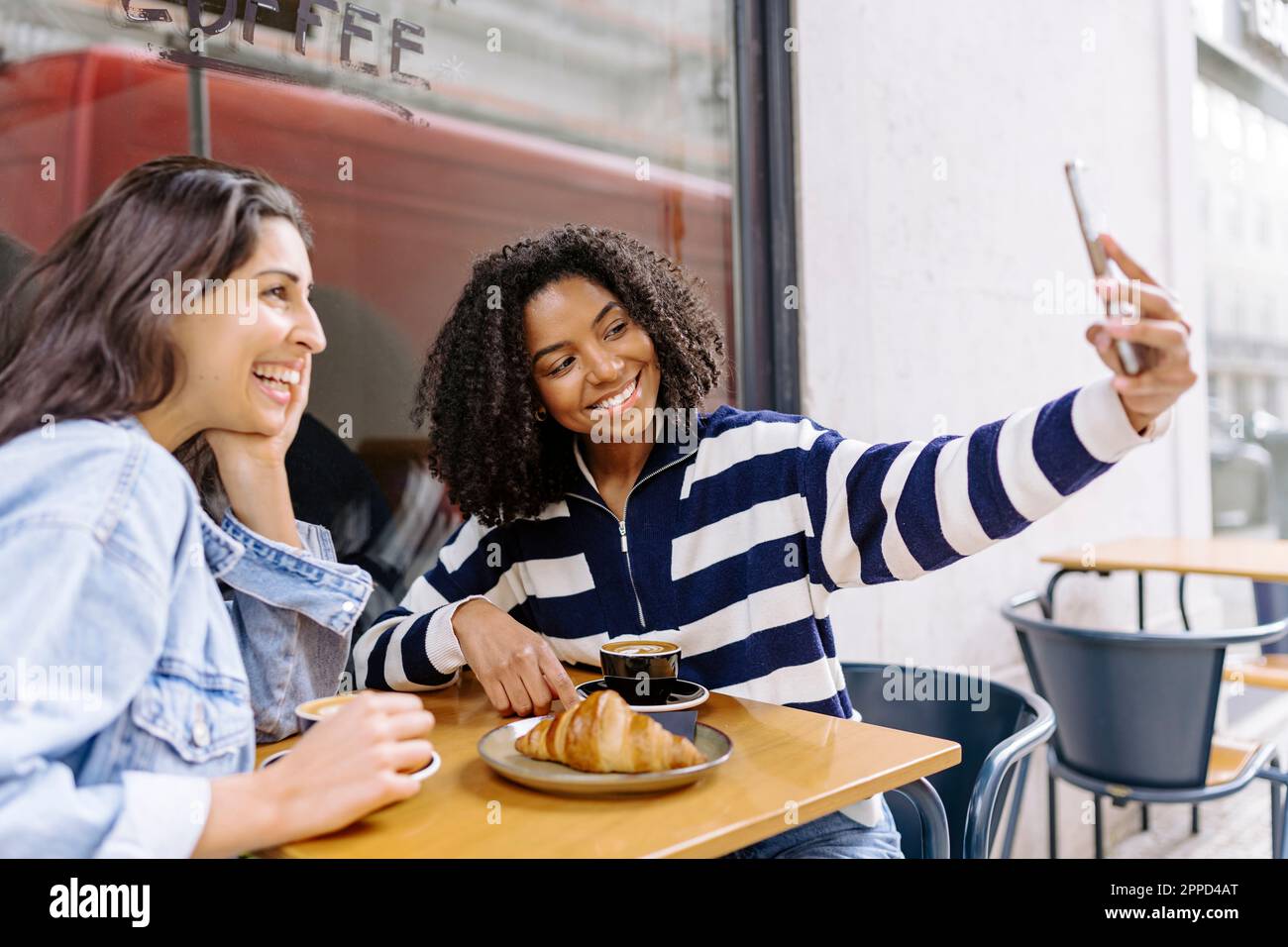 Smiling young woman taking selfie with friend at sidewalk cafe Stock ...