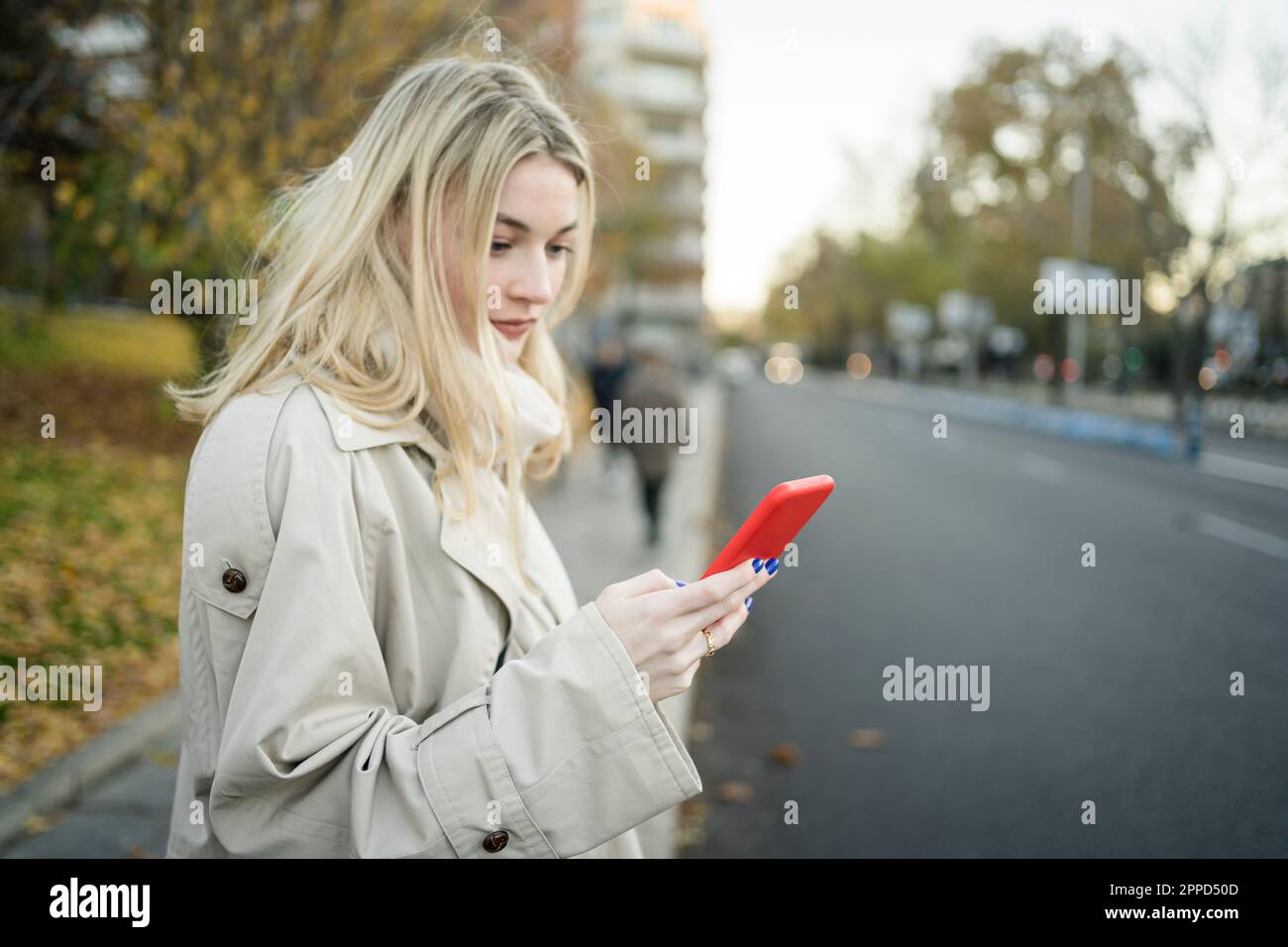 Blond woman using smart phone at sidewalk Stock Photo