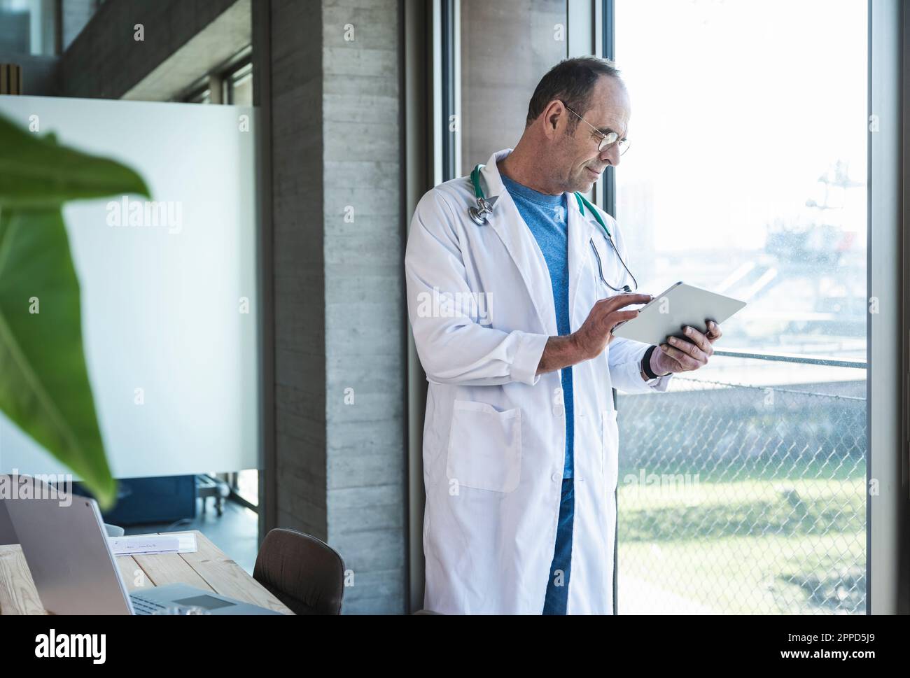 Doctor using tablet computer standing by window Stock Photo
