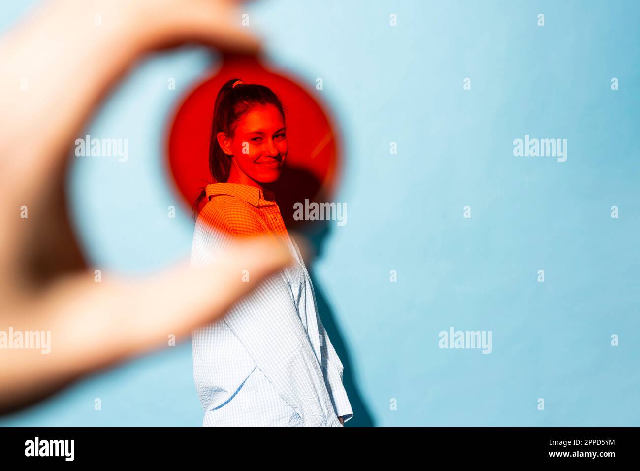 Smiling young woman seen through red lens filter against blue ...