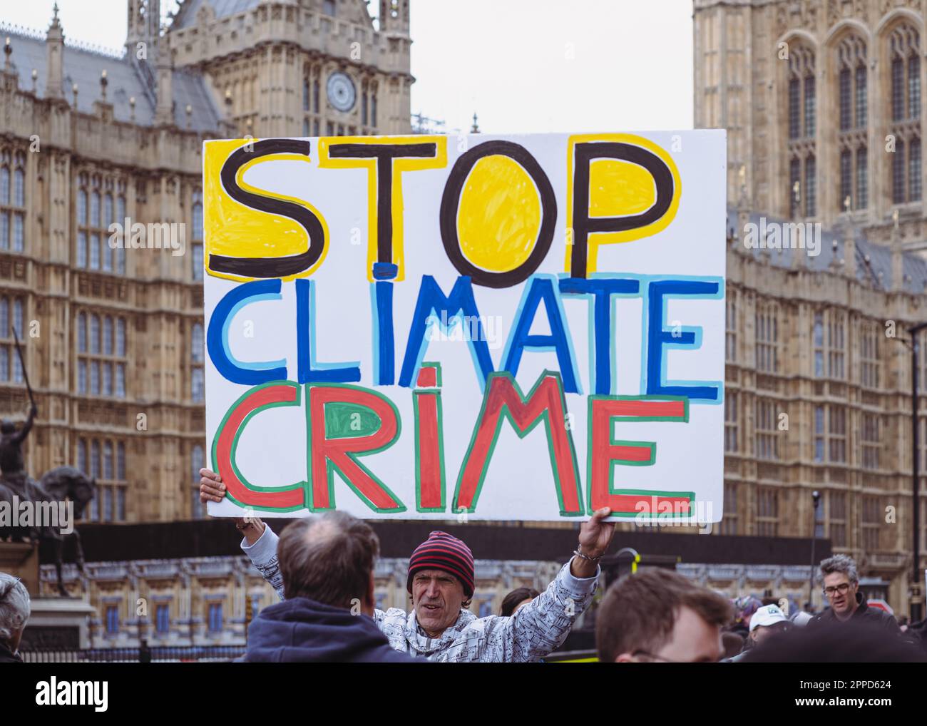 Man holds up large 'Stop Climate Crime' placard outside Palace of Westminster/Houses of Parliament, Extinction Rebellion protest, April 2023. London. Stock Photo