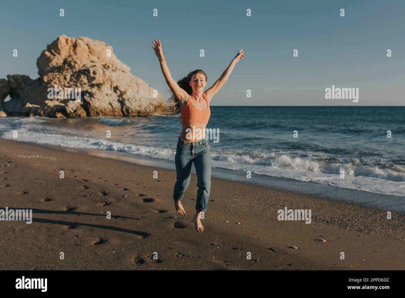 Cheerful woman jumping and running at beach Stock Photo