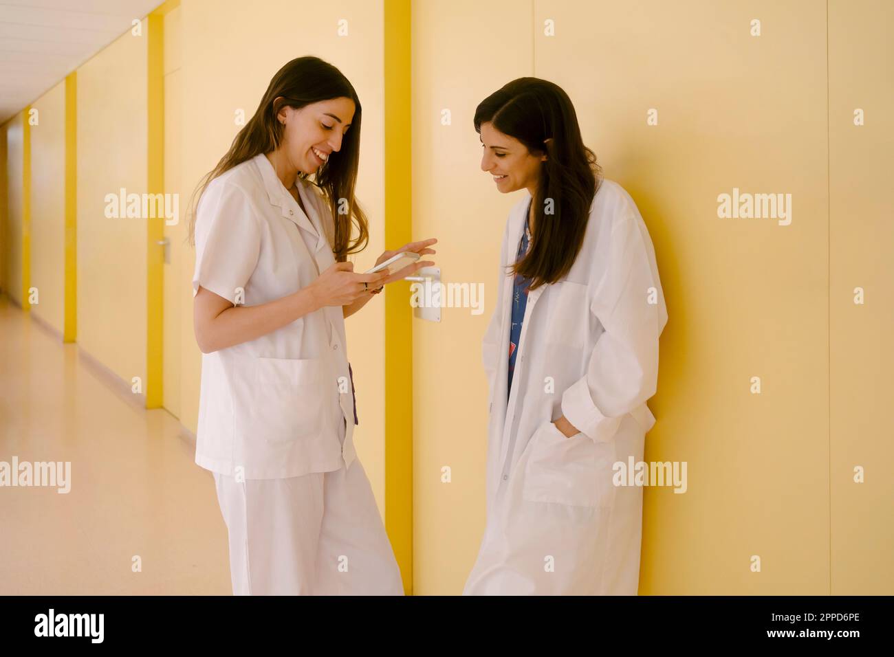 Smiling doctors sharing smart phone standing in corridor Stock Photo