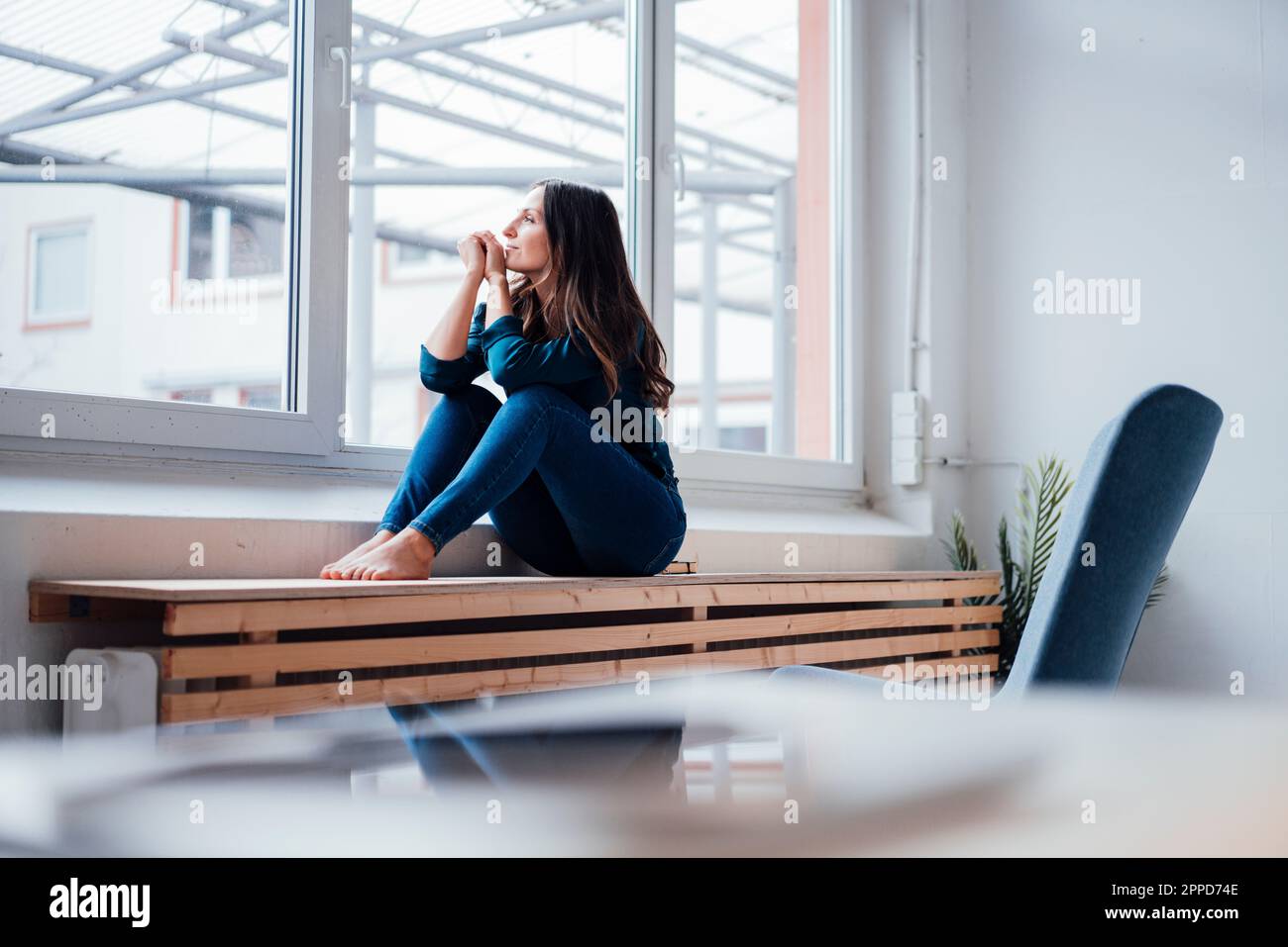 Thoughtful young woman looking through window Stock Photo