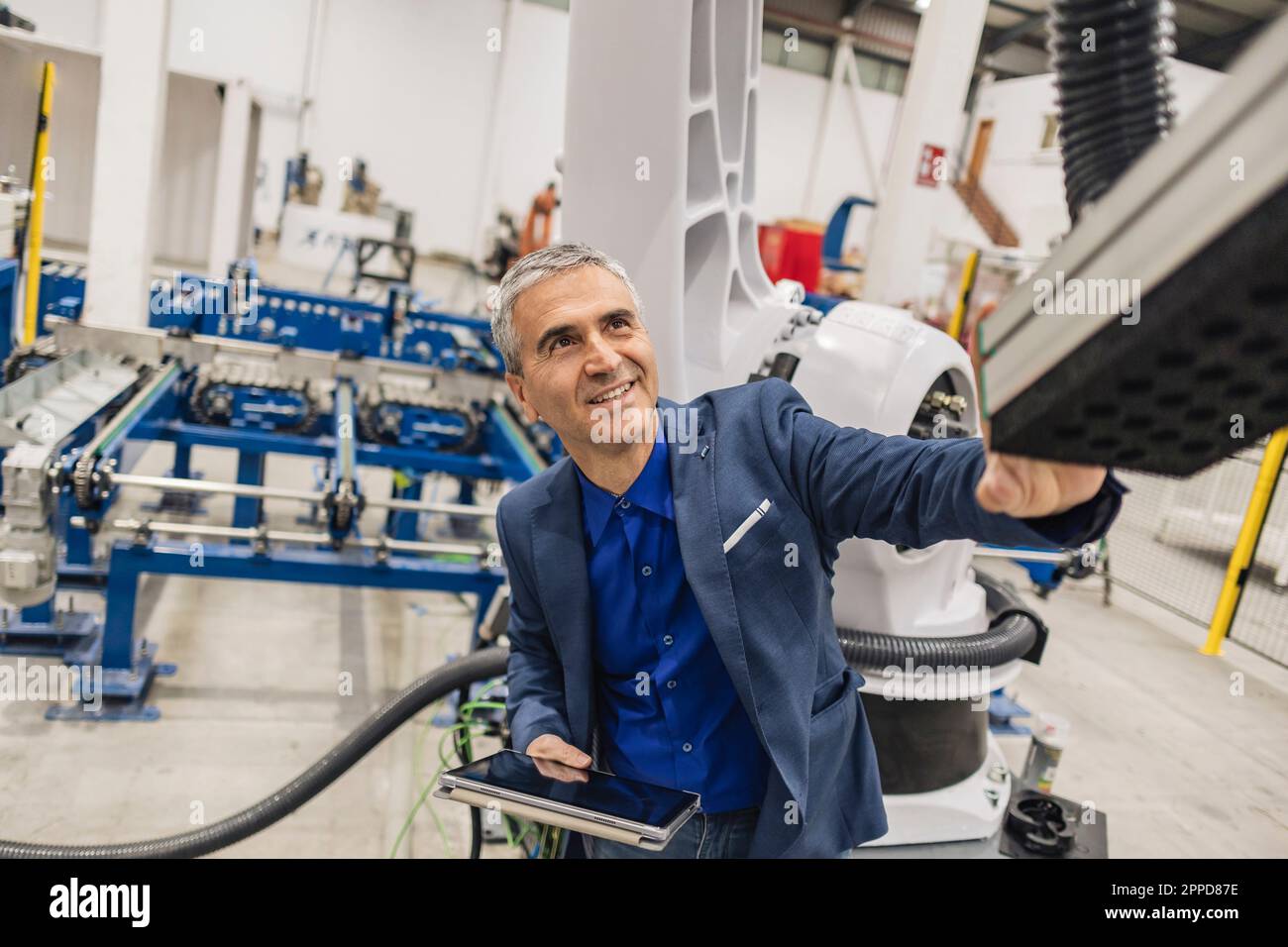 Smiling mature engineer with tablet PC touching robotic arm Stock Photo