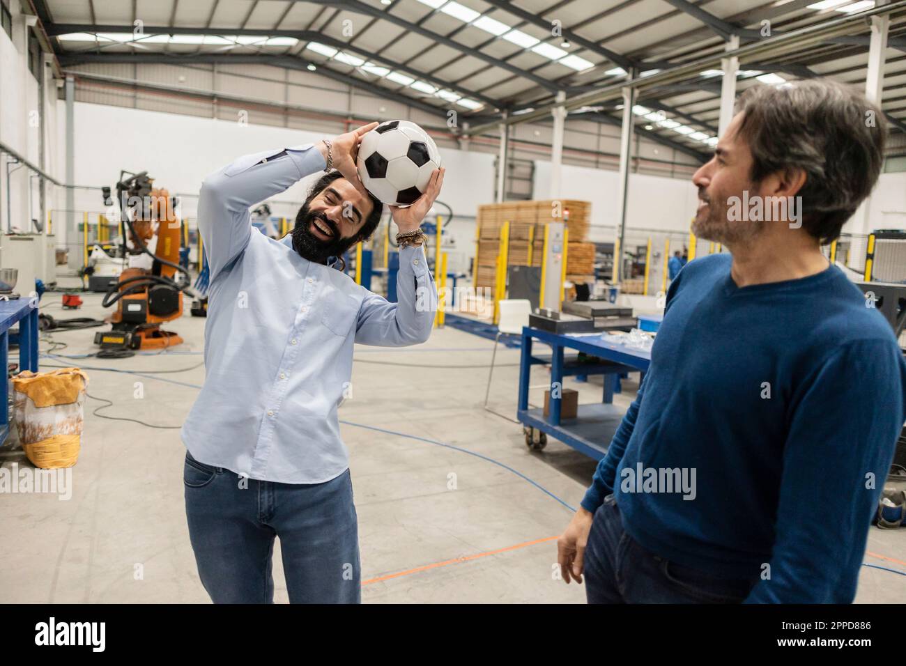 Happy engineers playing with soccer ball at industry Stock Photo