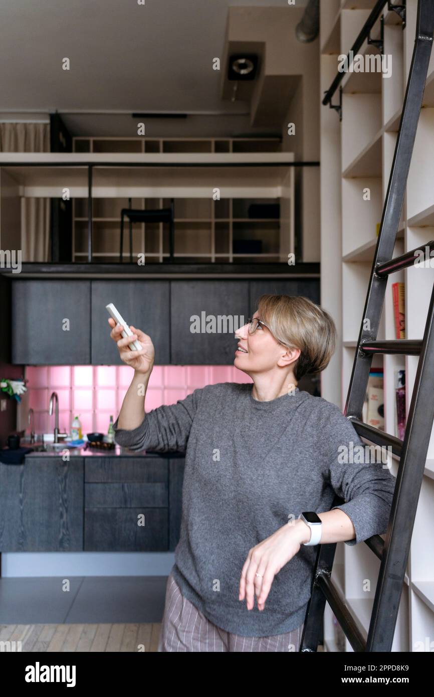 Woman using remote controller by ladder at home Stock Photo - Alamy