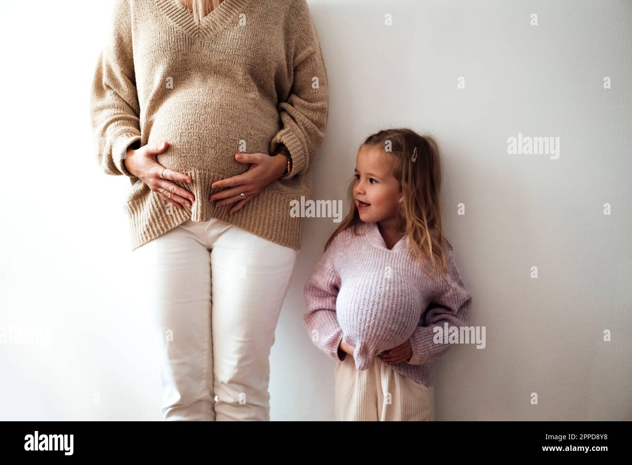 Daughter mimicking mother's pregnancy in front of wall Stock Photo Alamy