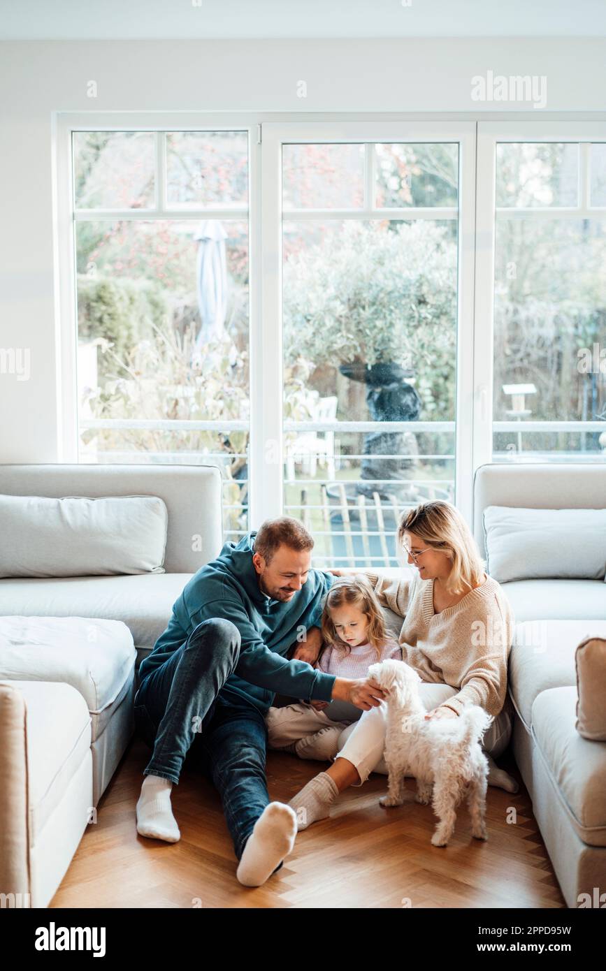 Smiling family with dog sitting on ground at home Stock Photo