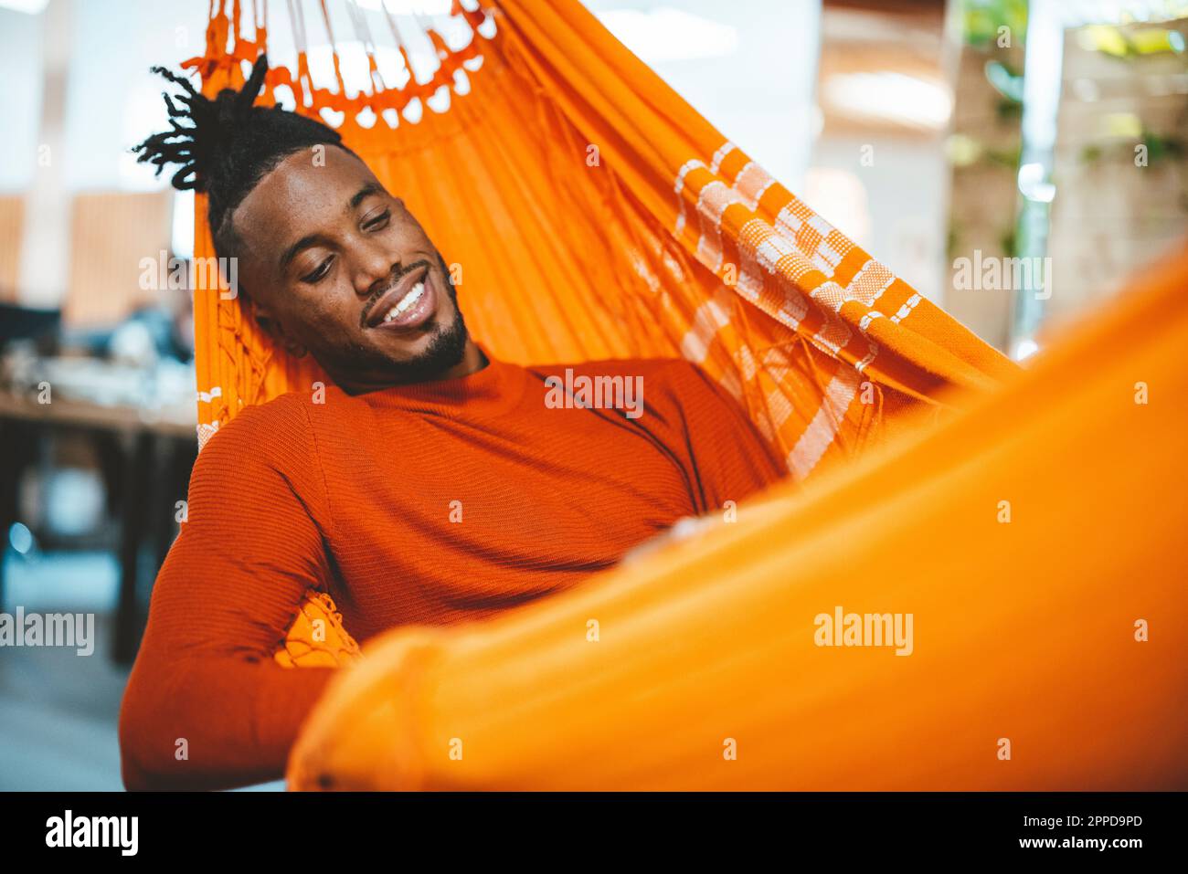 Smiling young businessman relaxing in hammock in office Stock Photo