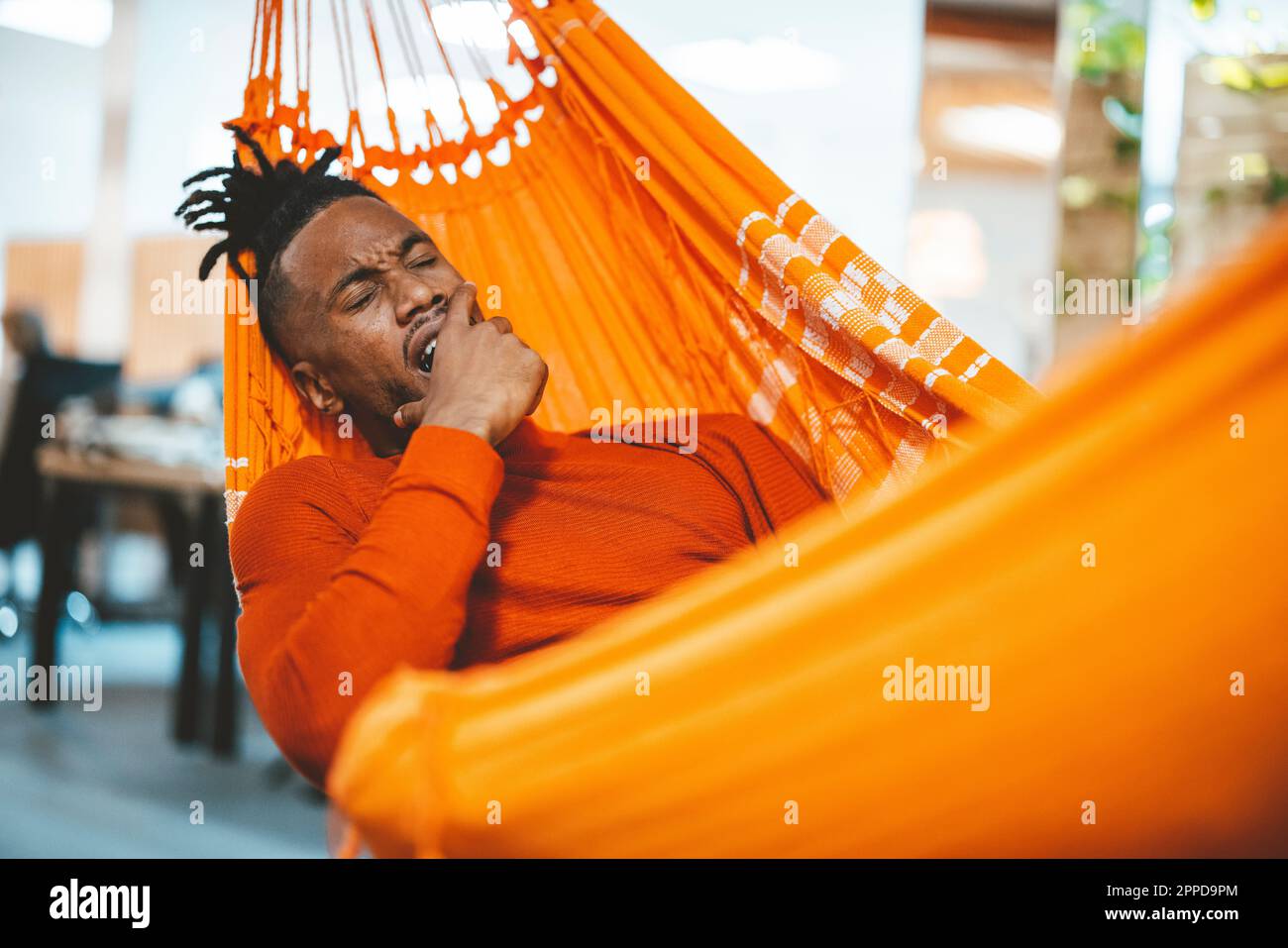 Tired businessman lying in hammock and yawning in office Stock Photo