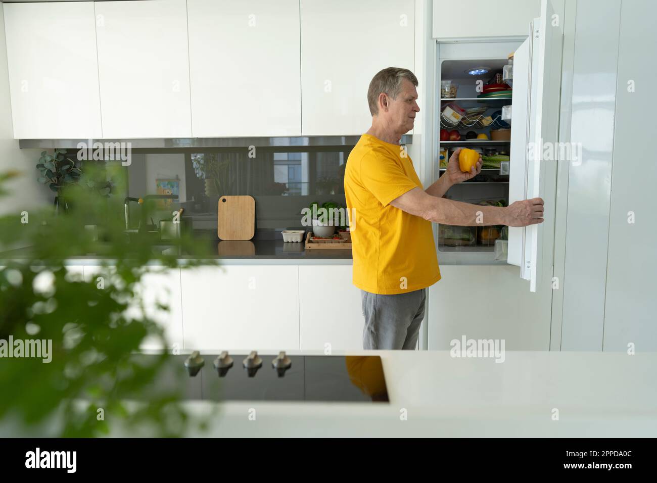 Senior man opening refrigerator door in kitchen at home Stock Photo
