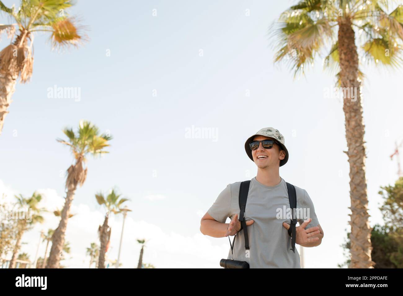 Happy man wearing hat standing under palm tree Stock Photo - Alamy