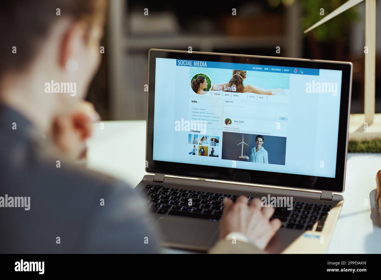 Seen from behind modern woman with laptop in modern office reading news ...