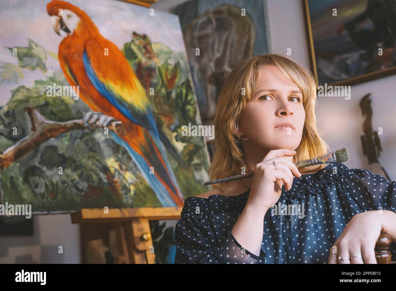 Painter holding paintbrush in front of bird painting Stock Photo