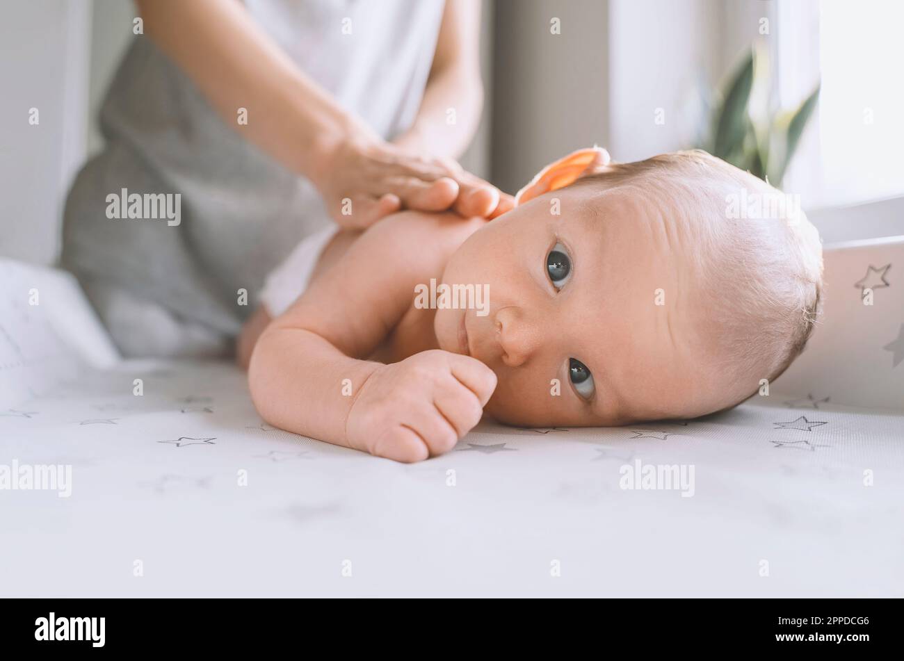 Baby boy lying on changing table with mother in background at home