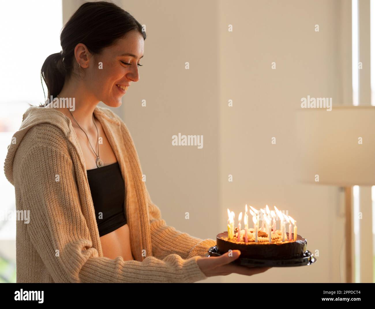 Smiling young woman holding birthday cake at home Stock Photo - Alamy