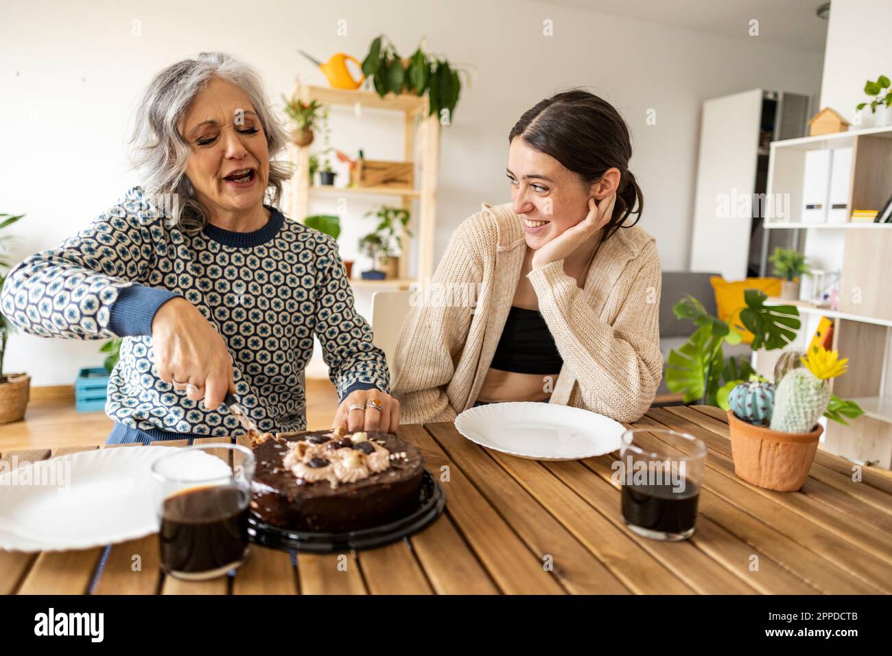 Mother cutting cake with daughter sitting at table Stock Photo
