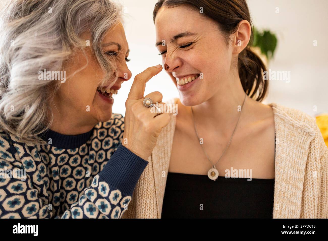 Happy mature woman applying chocolate on daughter's nose Stock Photo