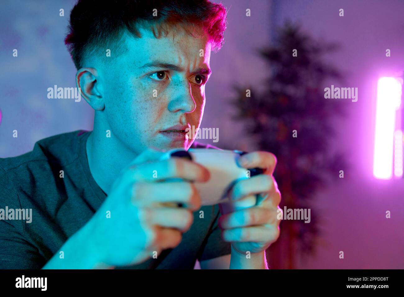 Young man concentrating with controller playing video game at home Stock Photo