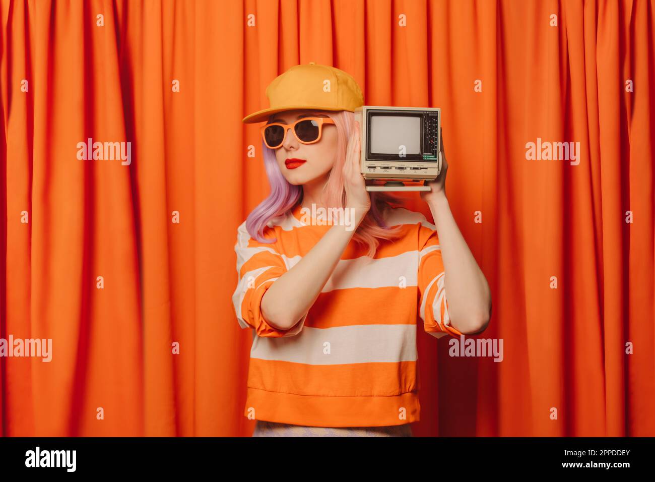 Woman holding retro style television set in front of orange curtain Stock Photo