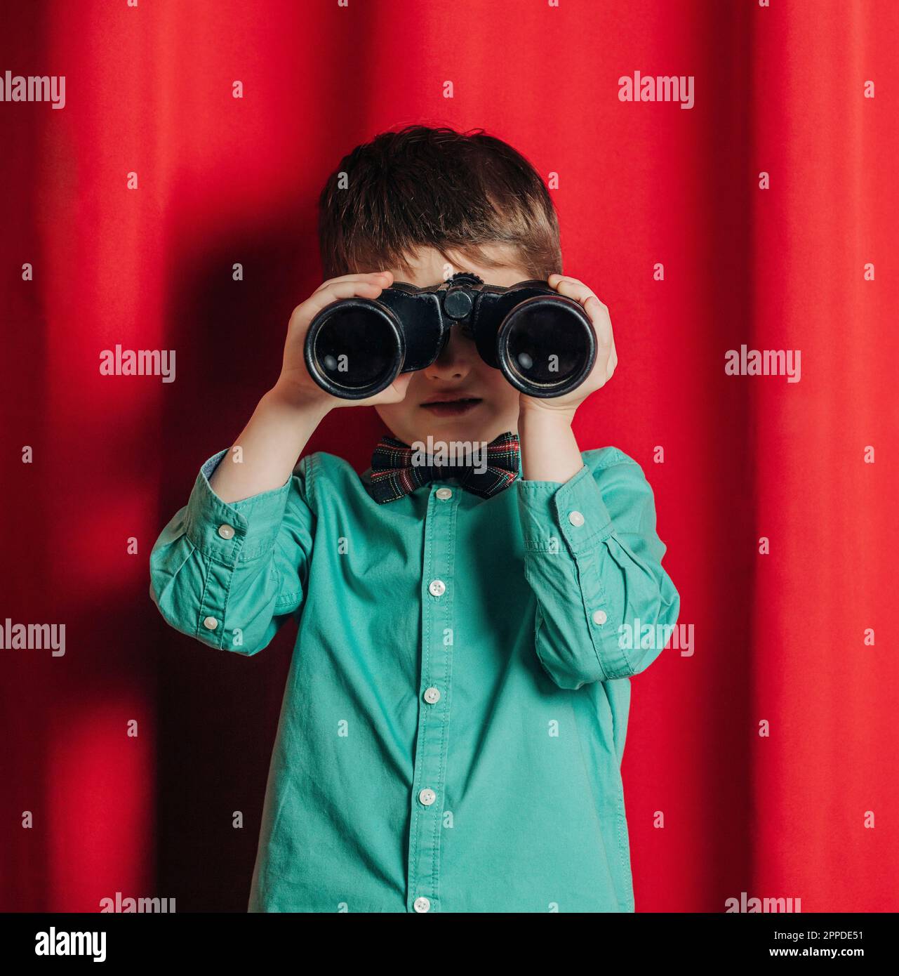 Boy looking through binoculars in front of curtain Stock Photo - Alamy