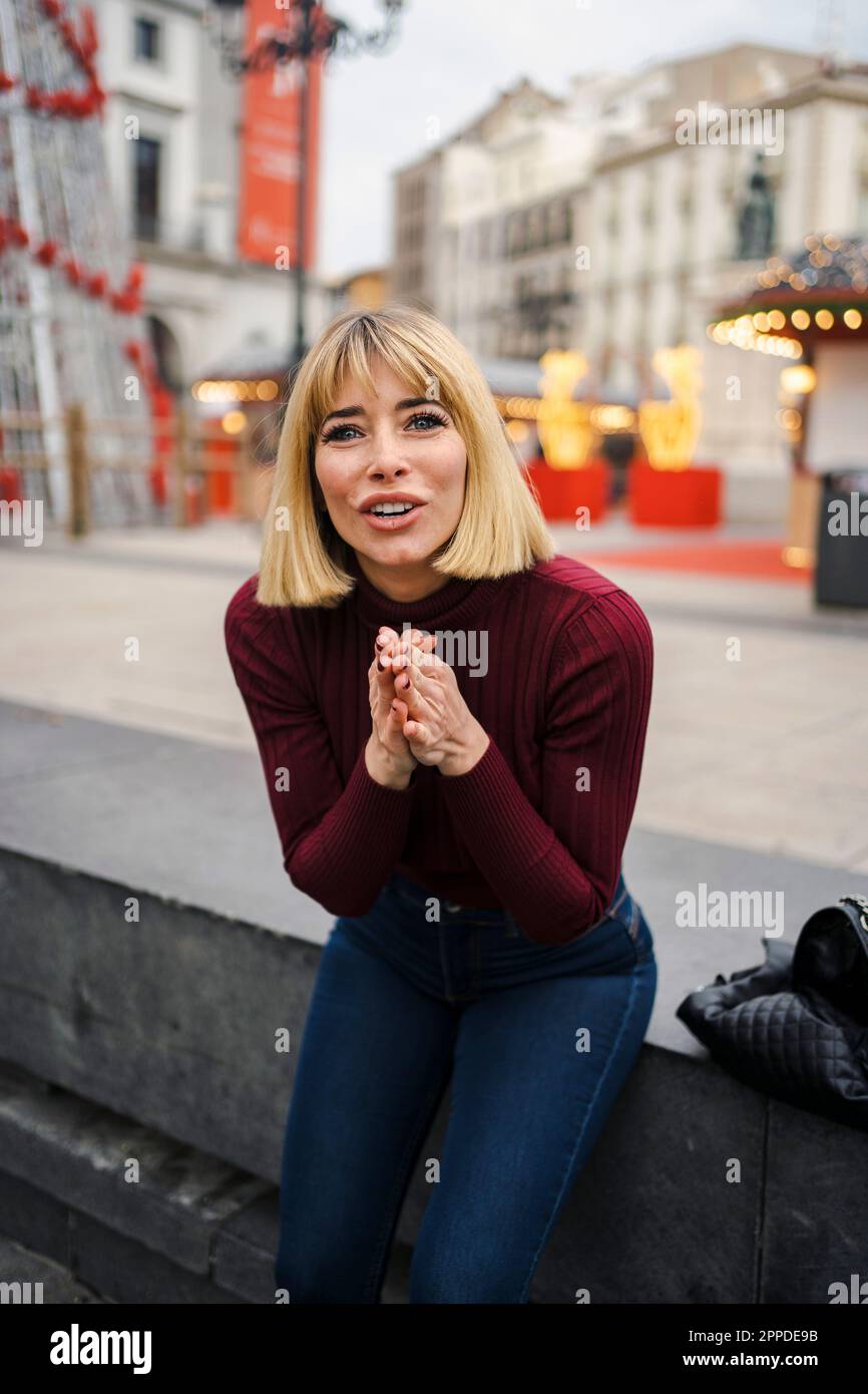 Woman pleading with hands clasped sitting on bench Stock Photo