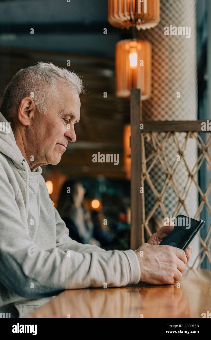 Senior man using smart phone sitting in cafe Stock Photo