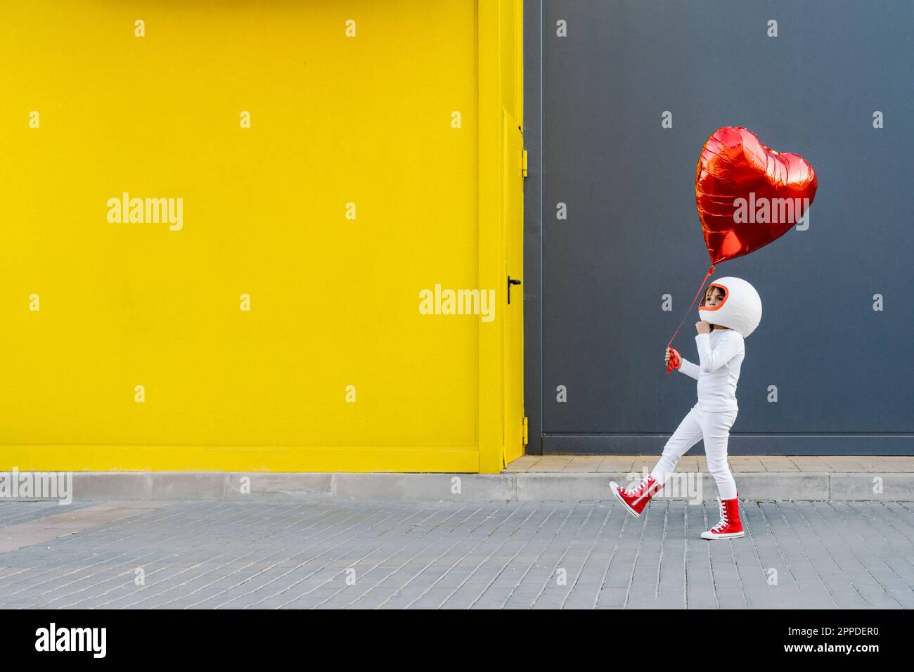 Girl holding heart shape balloon walking near yellow wall Stock Photo