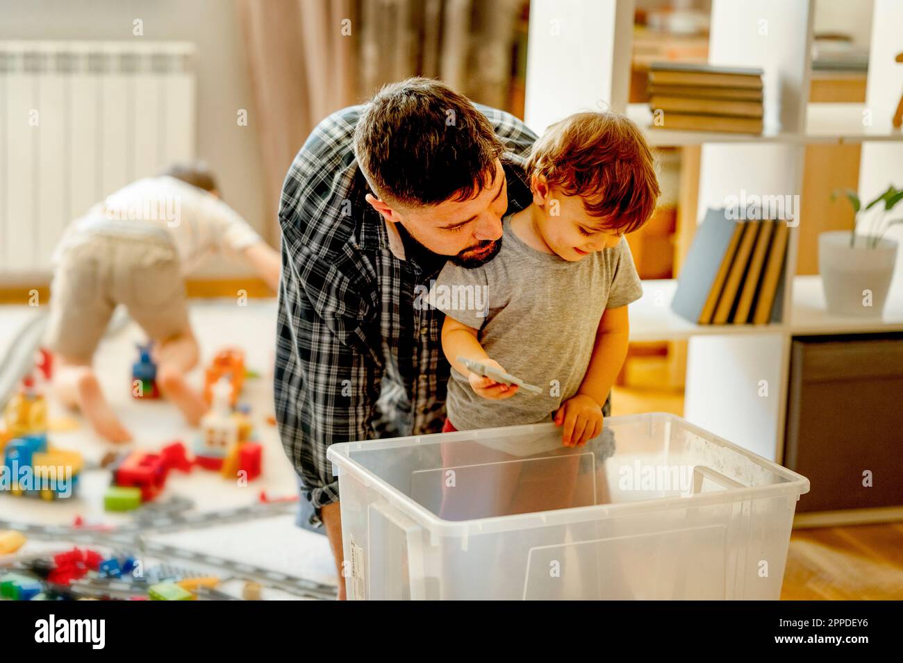 Father and son looking for toys in plastic container at home Stock Photo