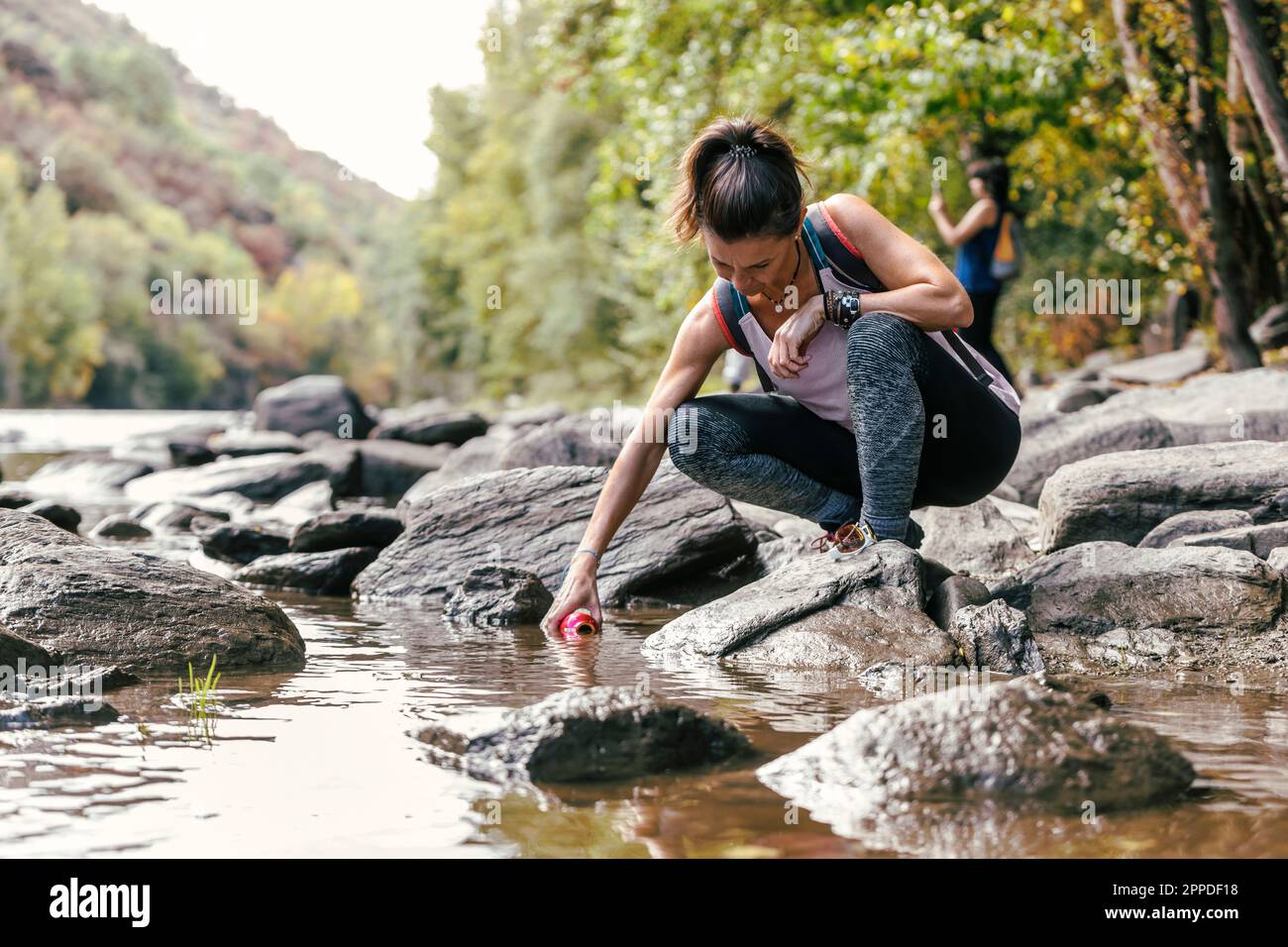 Mother crouching on rock filling water bottle from river Stock Photo