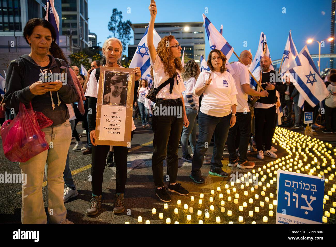 Tel Aviv, Israel. 22nd Apr, 2023. Bereaved family members hold placards with photos of their loved ones, next to thousands of 'Yom HaZikaron' candles for the Memorial Day of the Israeli fallen soldiers and terror attacks victims during an anti judicial overhaul demonstration in Tel Aviv. Credit: SOPA Images Limited/Alamy Live News Stock Photo