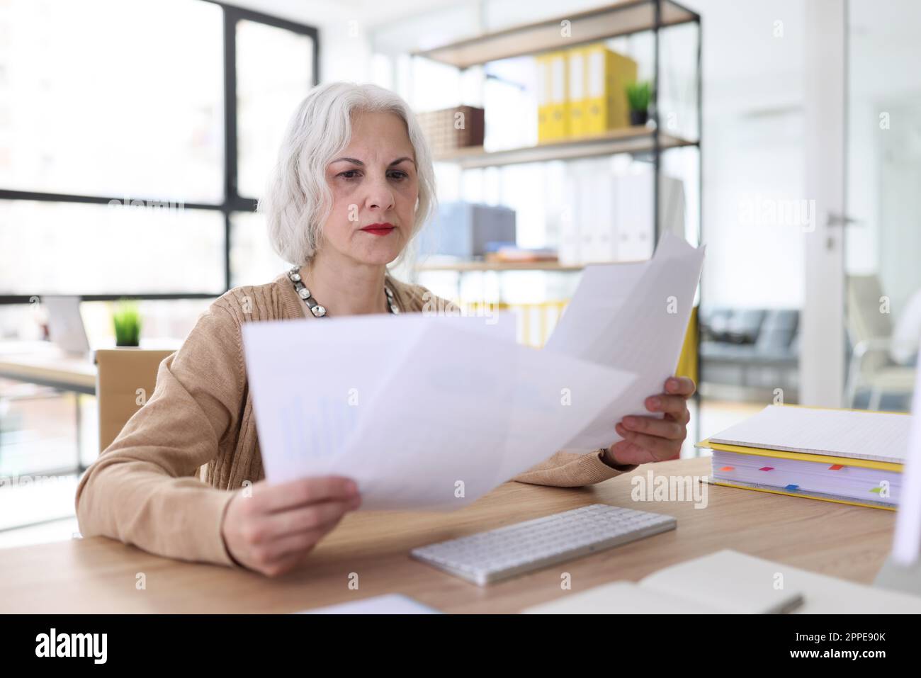 Serious grey haired woman studies reports sitting at desk Stock Photo
