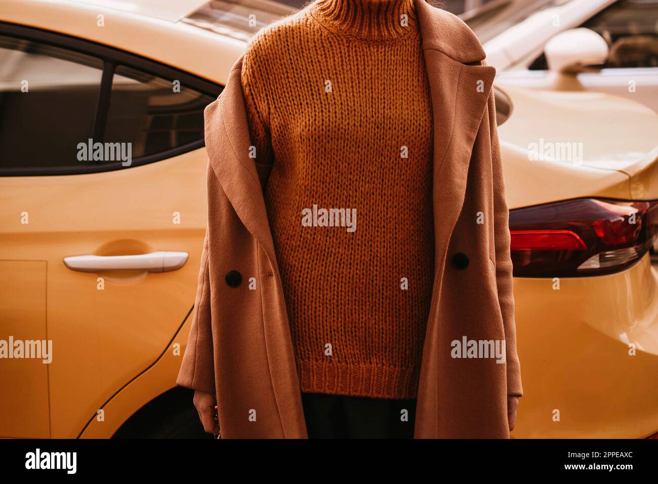 Female body in the orange warm knitting cozy sweater and long brown coat against the yellow taxi.. Urban autumn clothes street style concept Stock Photo