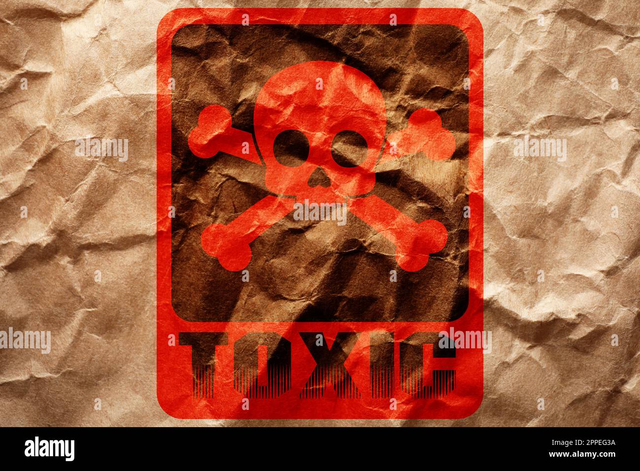 Hazard warning sign (skull-and-crossbones symbol and word TOXIC) on crumpled kraft paper, top view Stock Photo