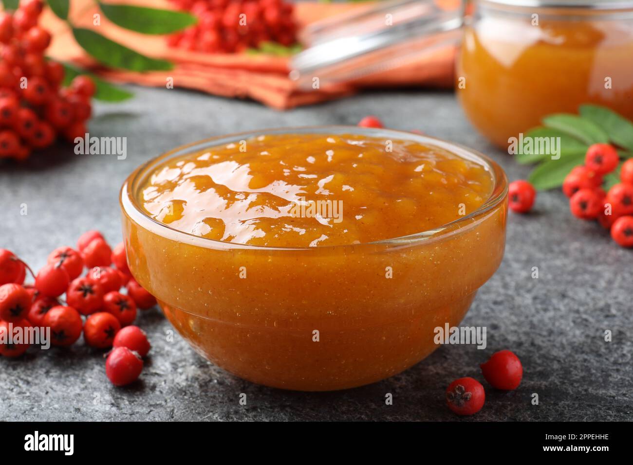 Delicious rowan jam in glass bowl and berries on grey table, closeup Stock Photo