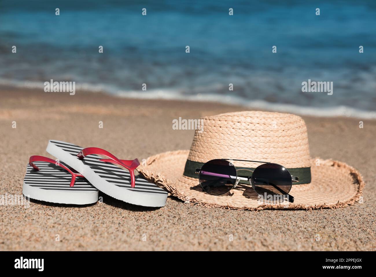 Striped flip flops, straw hat and sunglasses on sandy beach near sea ...