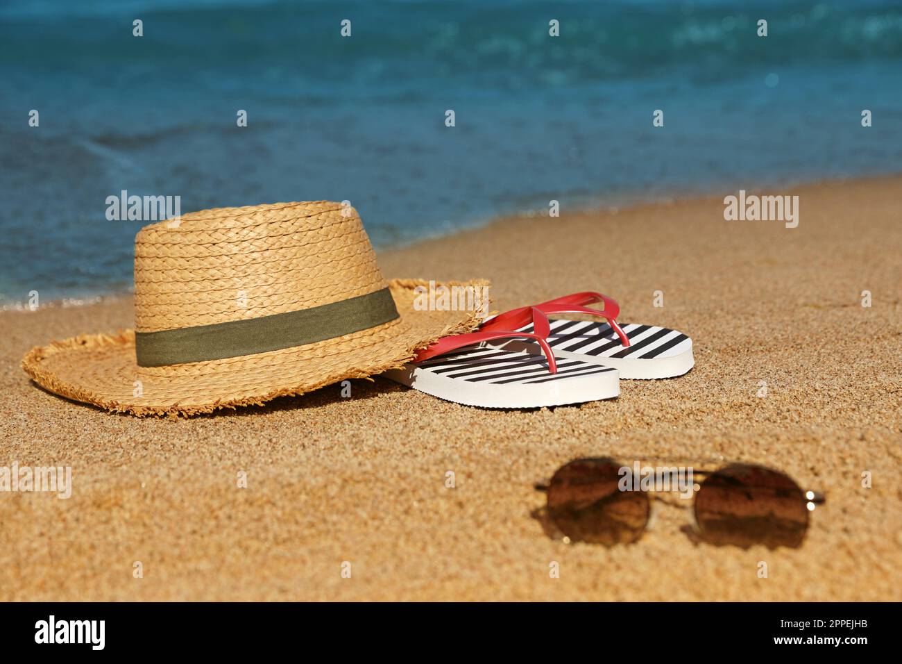 Stylish straw hat, sunglasses and striped flip flops on sandy beach ...