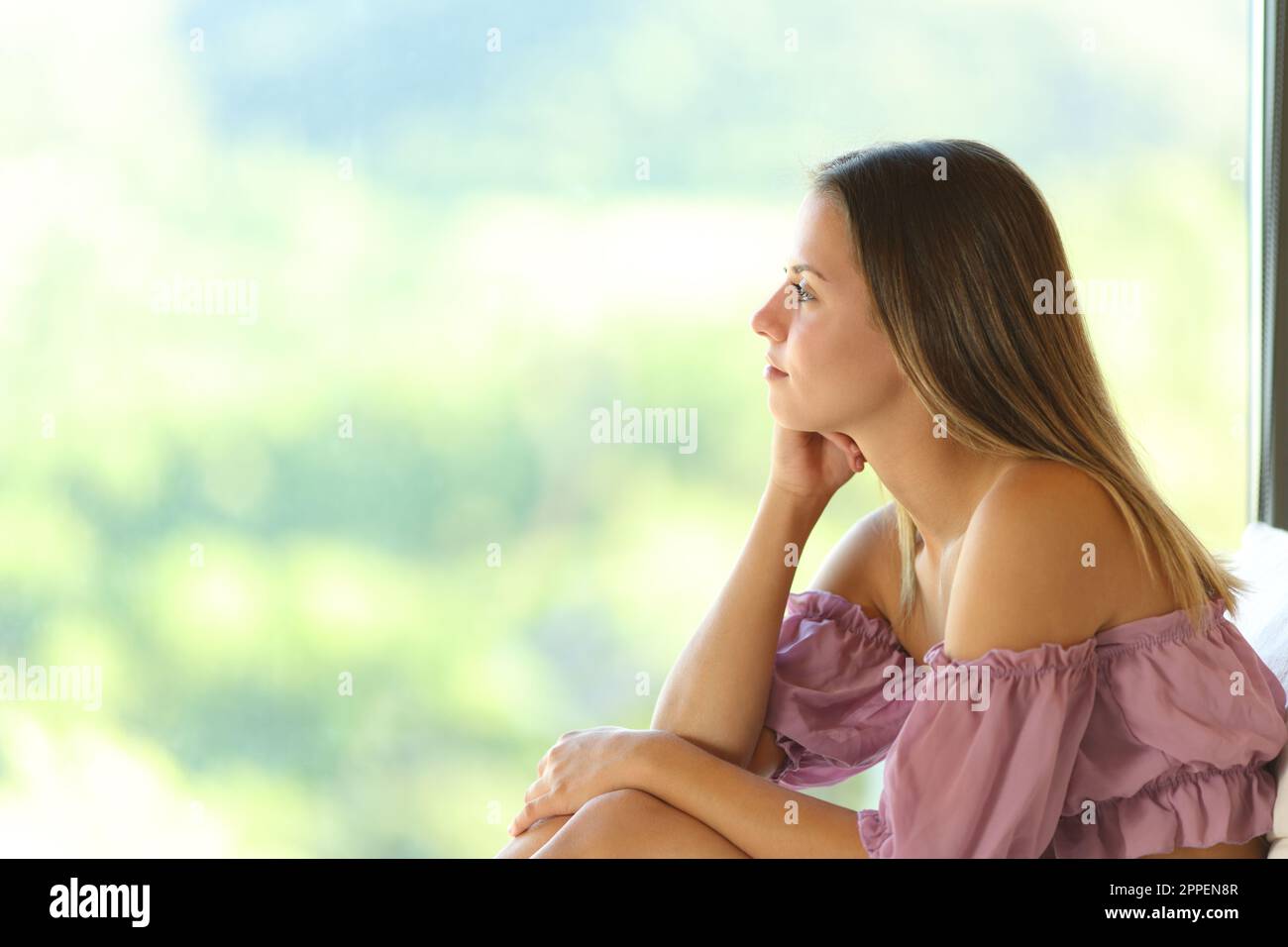 Pensive teen looking through a window inside a rural house Stock Photo