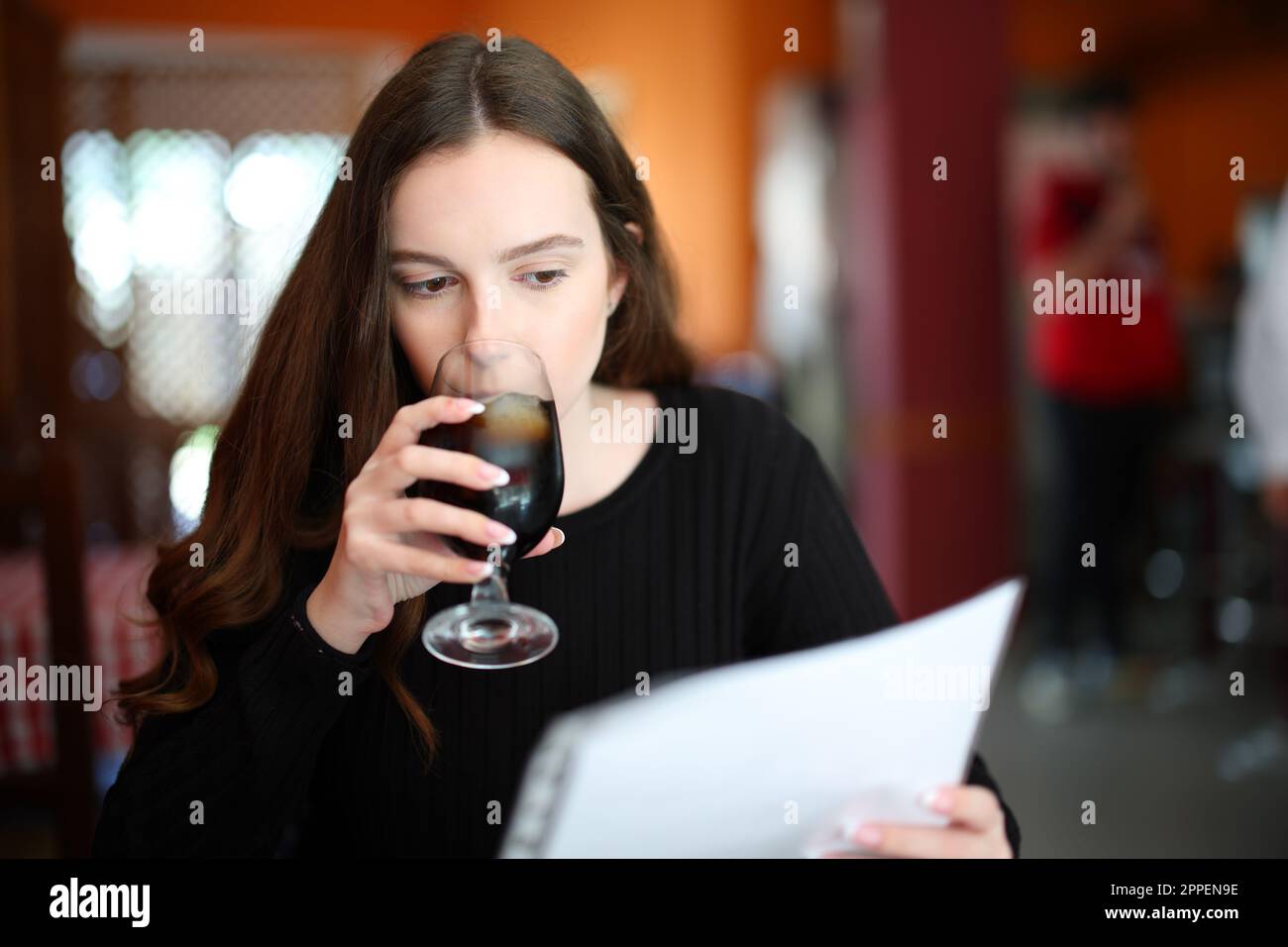Serious woman drinking and reading menu sitting in a bar Stock Photo