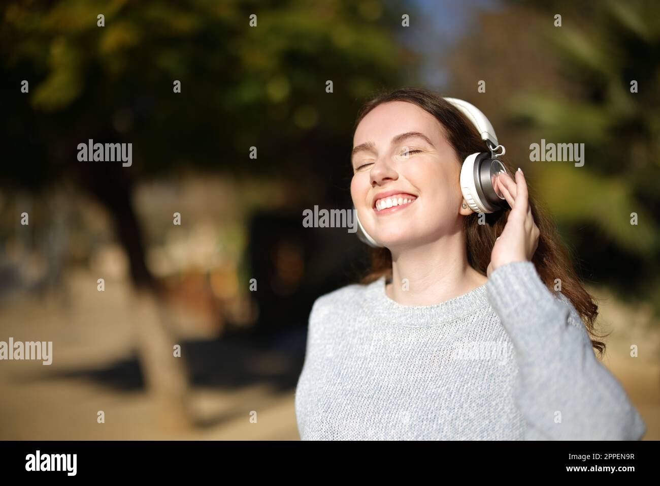 Happy woman listening music in a park with headphones a sunny day Stock Photo