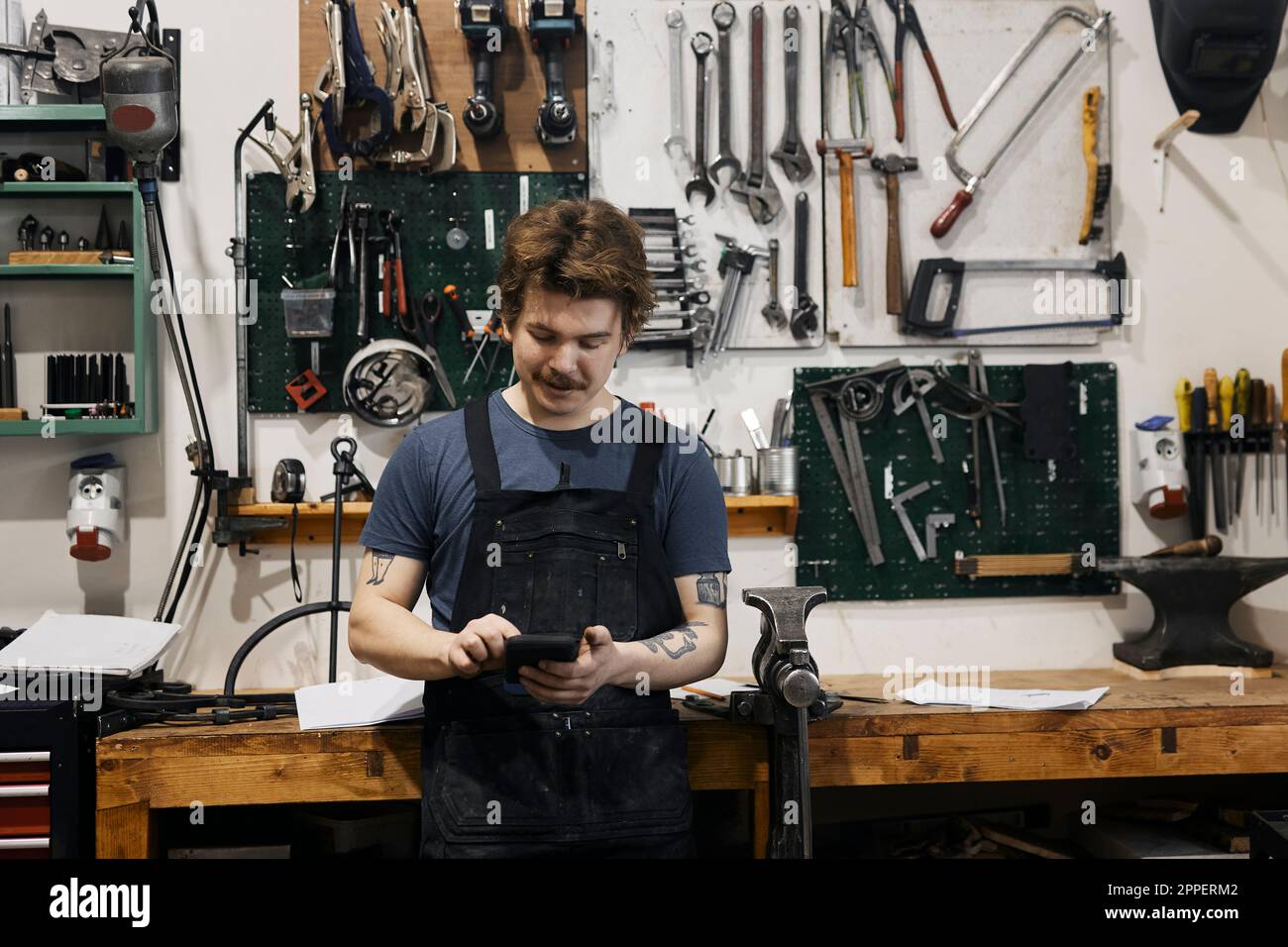 Blacksmith using smartphone in his workshop Stock Photo